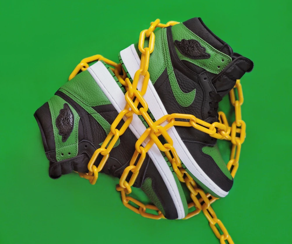 A pair of black & green Nike Air Jordan 1 with yellow chain wrapped around it